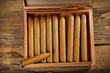 Cigars and burning one in box on wooden table, top view