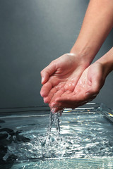 Obraz na płótnie Canvas Female hands with water splashing on dark background