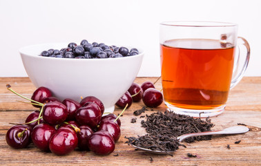 cup of tea, sweet cherry and blueberry in white bowl on a wooden