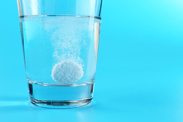 Pill in glass of water on blue background