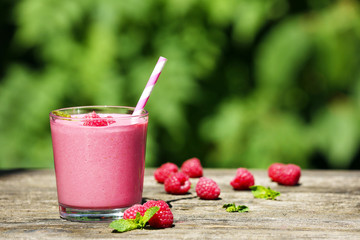 Glass of raspberry milk shake with berries on bright background