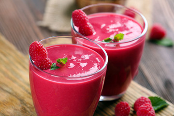 Glasses of raspberry milk shake with berries on wooden table close up