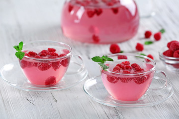 Cups and teapot of raspberry drink with berries on wooden table close up