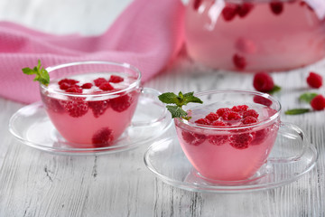 Cups and teapot of raspberry drink with berries on wooden table close up