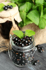 Ripe blackcurrant in glass jar and tasty jam on wooden background