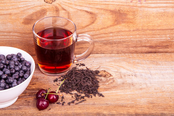 cup of tea, sweet cherry and blueberry in white bowl on a wooden