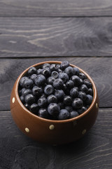 Brown dotted ceramic bowl filled with bilberries, rustic style. Wooden table  striped blue white towel background, homely. Vertical.
