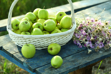 Green apples with bouquet of wildflowers on wooden table, closeup