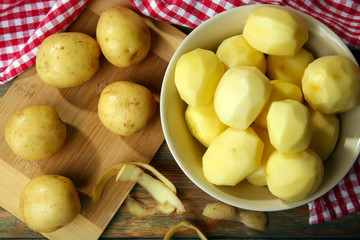 Peeled new potatoes in bowl on wooden table with napkin, top view