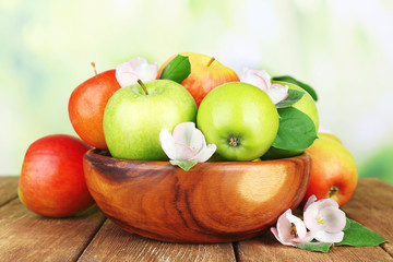 Fresh apples with apple blossom in bowl, on wooden table, on nature background