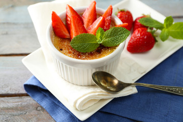 Creme brulee dessert with fresh strawberry berries on napkin, on color wooden background