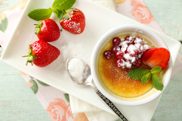 Creme brulee dessert with fresh strawberries and mint leaves, on color wooden background