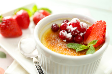 Creme brulee dessert with fresh strawberries and mint leaves, on color wooden background
