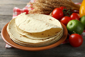 Stack of homemade whole wheat flour tortilla and vegetables on plate, on wooden table background