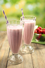 Glasses of milkshake with strawberries on bright background