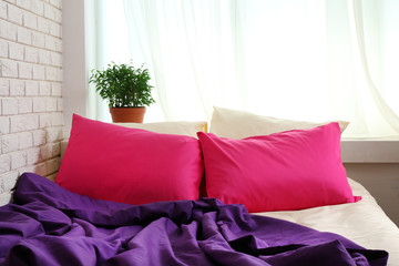 Comfortable bed with pink pillows and purple blanket in bedroom