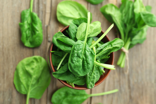 Bowl of fresh spinach leaves on wooden table, closeup
