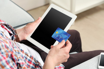 Man holding credit card and tablet on sofa in room