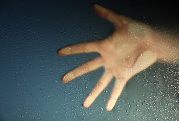 Fototapeta na wymiar Female hand behind wet glass, close-up