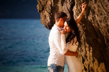 brunette bride leans on large cliff in water