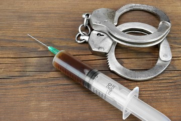 Medical Syringe And Handcuffs On The Wooden Table