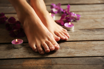 Obraz na płótnie Canvas Female feet at spa pedicure procedure with flowers and candlelight on wooden background