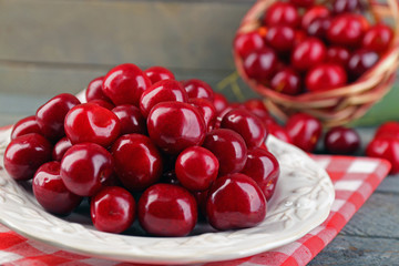 Sweet cherries with green leaves on plate, on wooden background