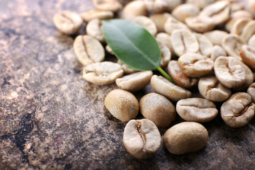 Heap of green coffee beans with leaf on table close up