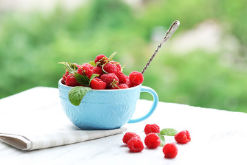 Fresh raspberries in cup on wooden table on blurred nature background