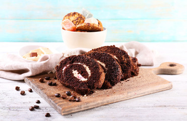 Delicious chocolate roll on cutting board on wooden background
