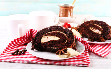 Delicious chocolate roll in white saucer on wooden table with checkered napkin, closeup