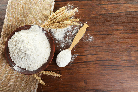 Bowl of whole flour with wheat ears on wooden table, top view