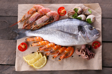 Dorado fish and other ingredients on parchment on wooden table, top view
