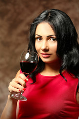 Pretty young woman with wineglass on brown background
