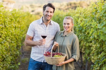 Two young happy vintners holding a basket of grapes and a glass 