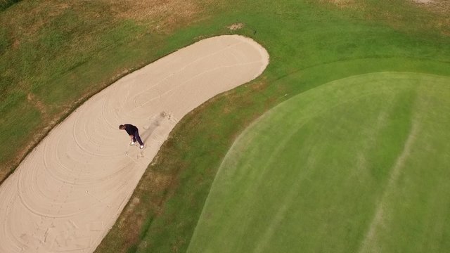 Golf player is hitting the golf ball out of the sand trap filmed from above by a drone.