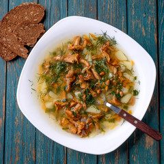 Soup with chanterelles, herbs and potatoes on wooden background.