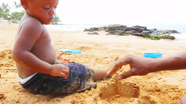 Black toddler playing in sand on a beach with his father