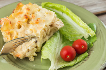 horizontal close up image of a prepared dinner of chicken lasagna with lettuce and two cherry tomatoes on a green glass plate filling the whole frame.