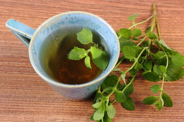 Fresh lemon balm and cup of herbal drink on wooden table