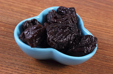 Dried plums in blue bowl on wooden table, healthy food