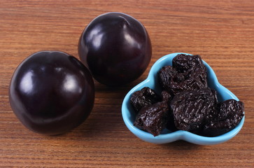 Fresh and dried plums in blue bowl on wooden table, healthy food