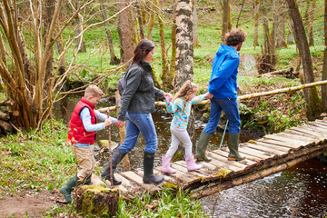Naklejka na ściany i meble Family Walking Across Wooden Bridge Over Stream In Forest