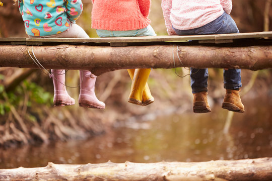 Close Up Of Children's Feet Dangling From Wooden Bridge