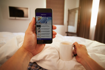Man In Bed Looking At News Website On Mobile Phone