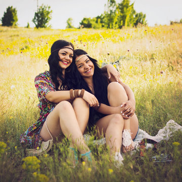 Two happy boho sisters hugging sitting outdoors