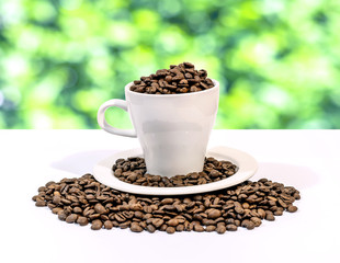 Coffee beans in a white coffee cup on a white and green bokeh ba