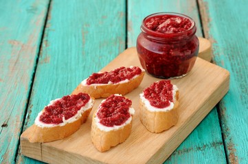 Homemade sweet raspberry jam in glass jar with four toasts with
