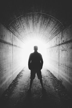Young man stands in dark tunnel and looks in the glowing end, bl