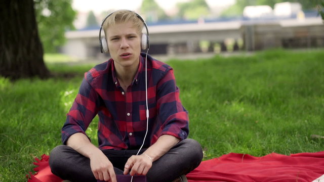 Boy listening music in the park and singing to the camera

